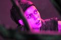 Senua from Hellblade 2 bathed with purple light on her face looking through tree branches .